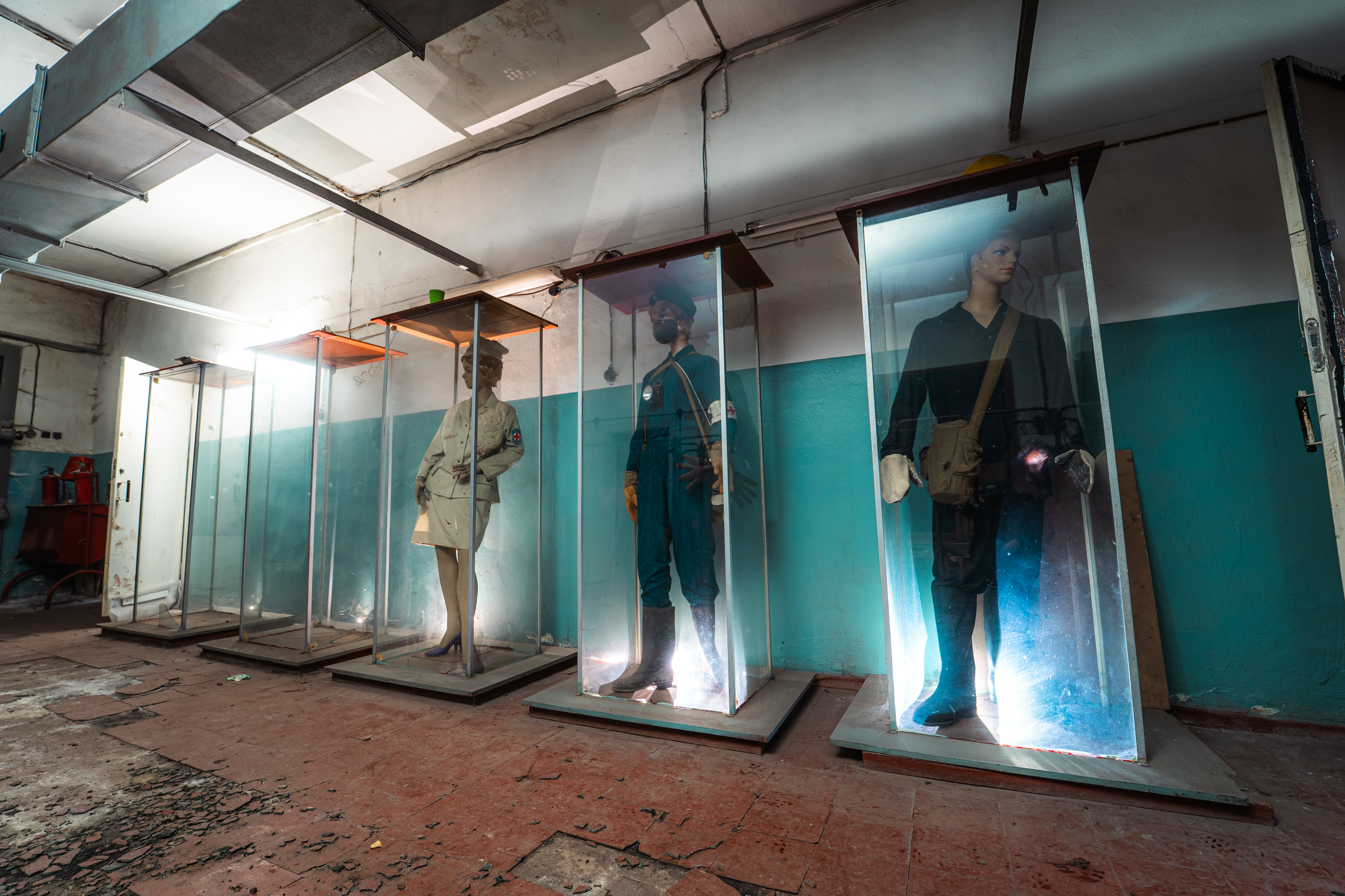 A dimly lit room featuring glass display cases with mannequins in historical uniforms, set against teal-painted walls and a worn wooden floor.