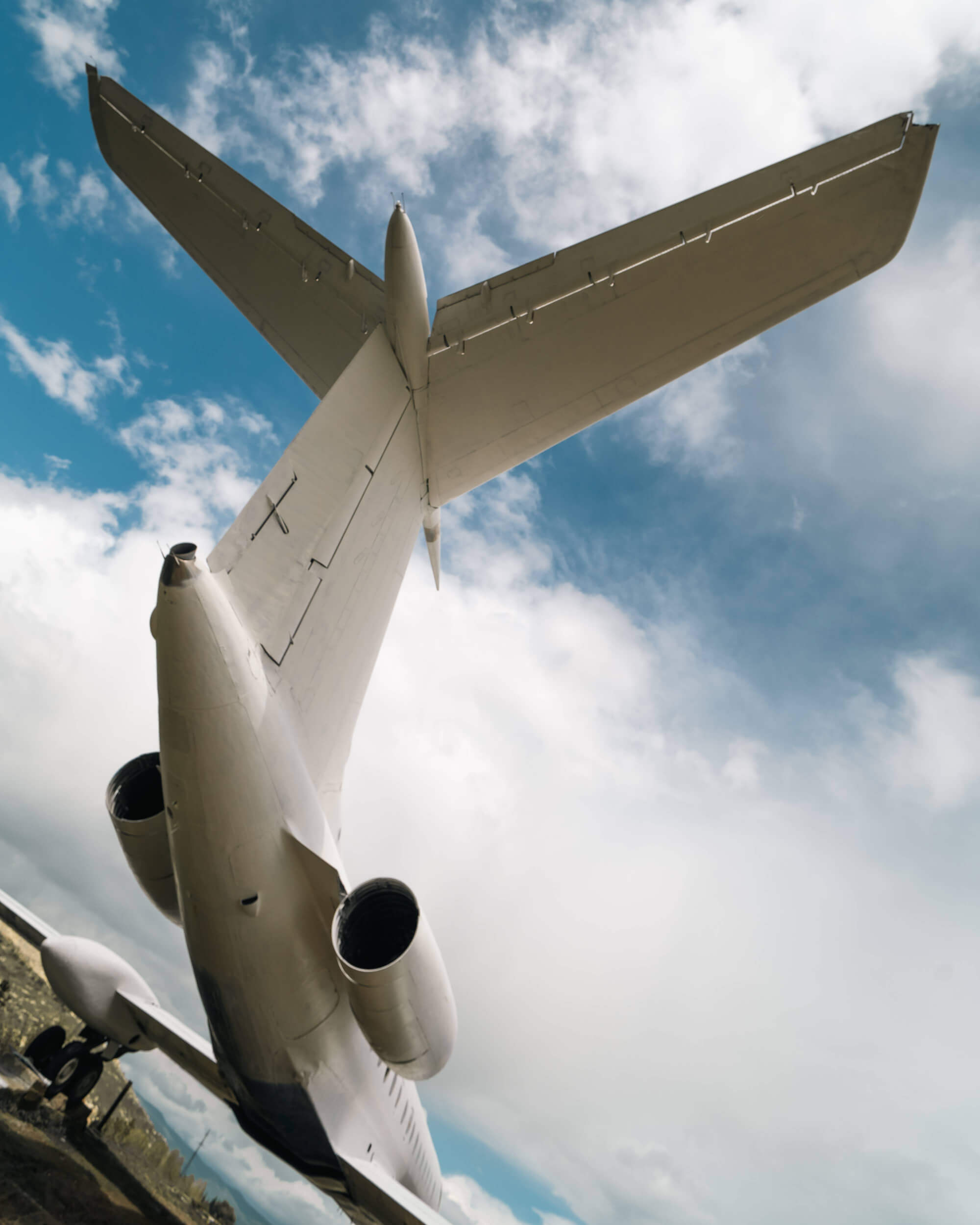 Low-angle shot of an airplane tail against a blue sky with clouds, emphasizing the aircraft's wingspan and engines.