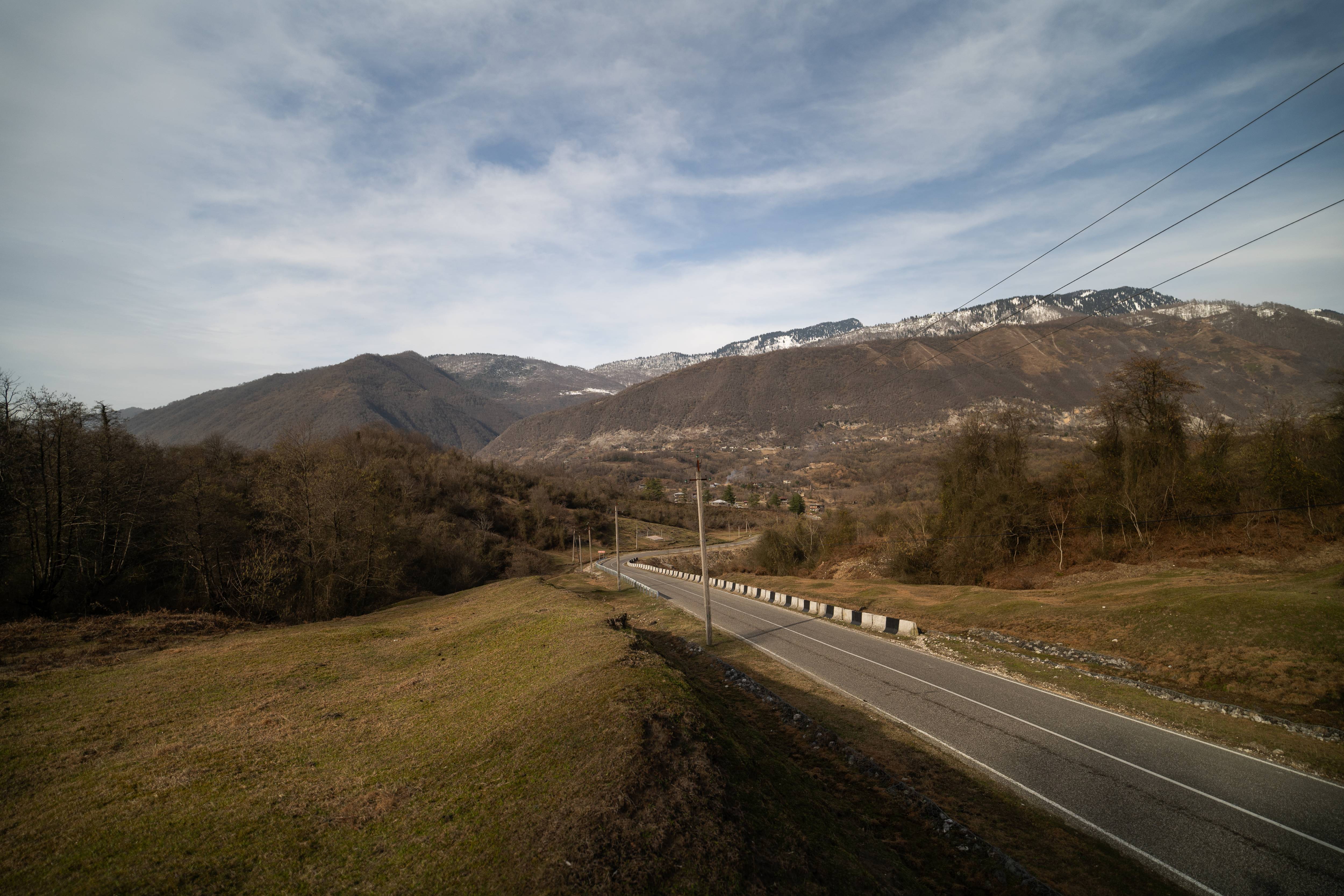 A winding road through green hills leading to snow-capped mountains under an overcast sky.