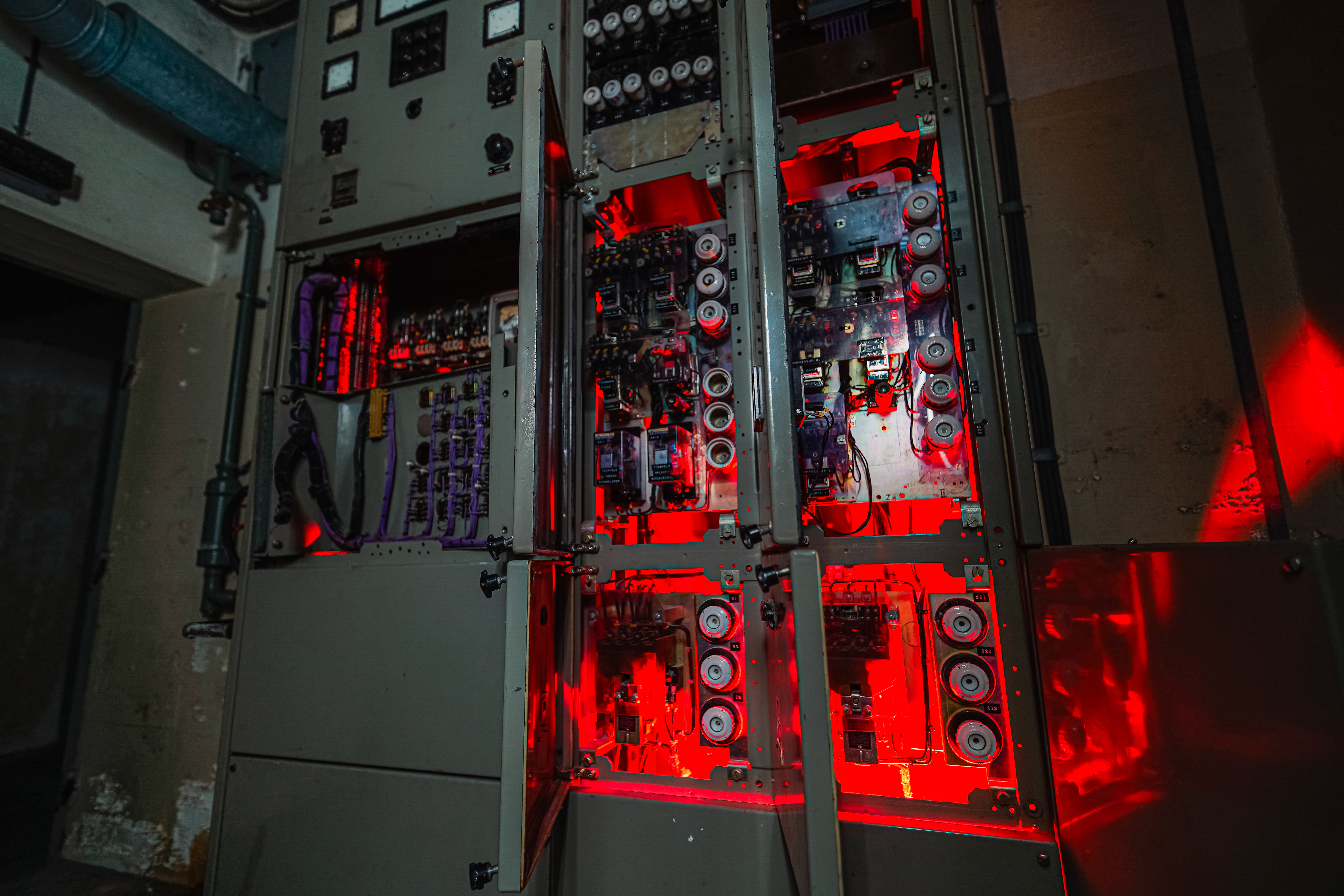 Close-up of an industrial electrical panel with open compartments displaying glowing circuits and devices illuminated by red light.