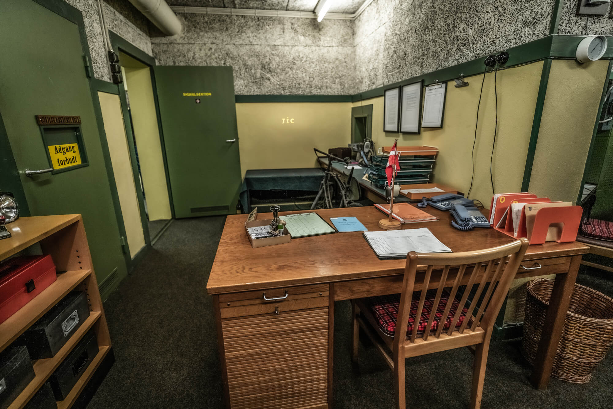 A wooden desk with papers and office supplies in a vintage office. Green doors and textured walls create a retro atmosphere.