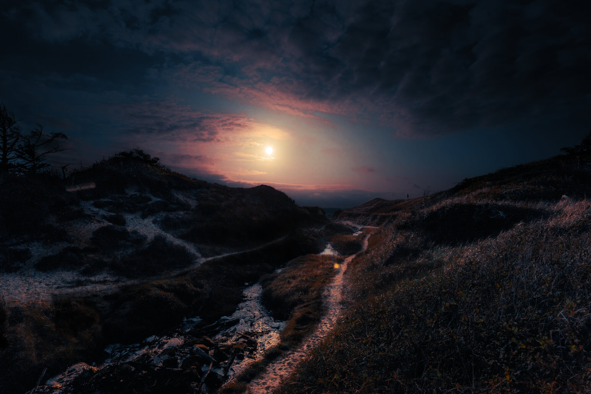 A serene landscape at twilight with rolling hills, a winding path, and a small stream reflecting the muted colors of the sky. The sun sets behind the hills, creating a tranquil and peaceful atmosphere.