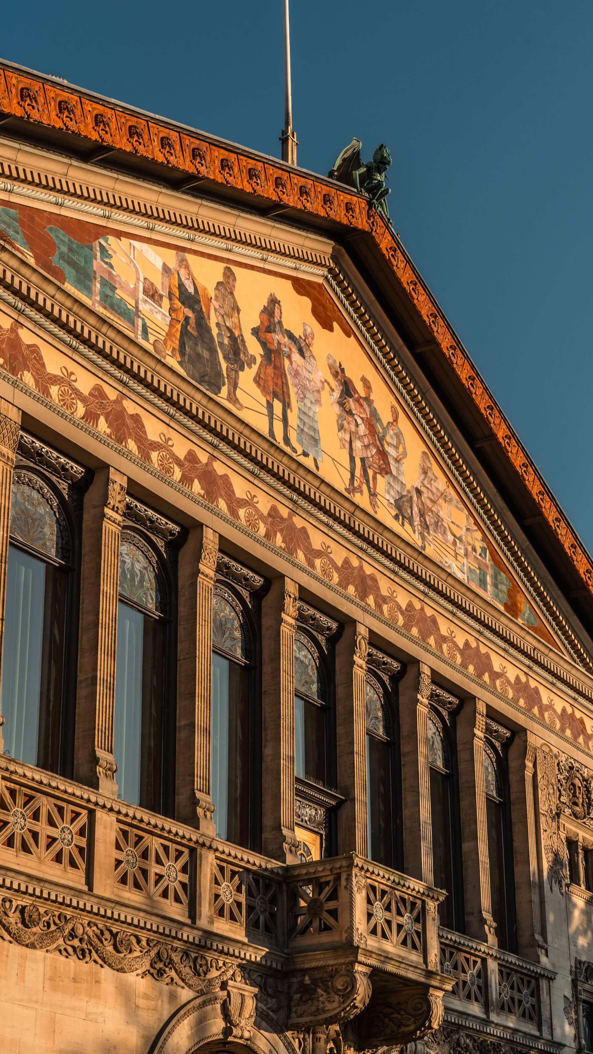 A close-up of a beautifully decorated building facade, featuring murals of historical figures and intricate architectural details, with warm evening light and a clear blue sky.