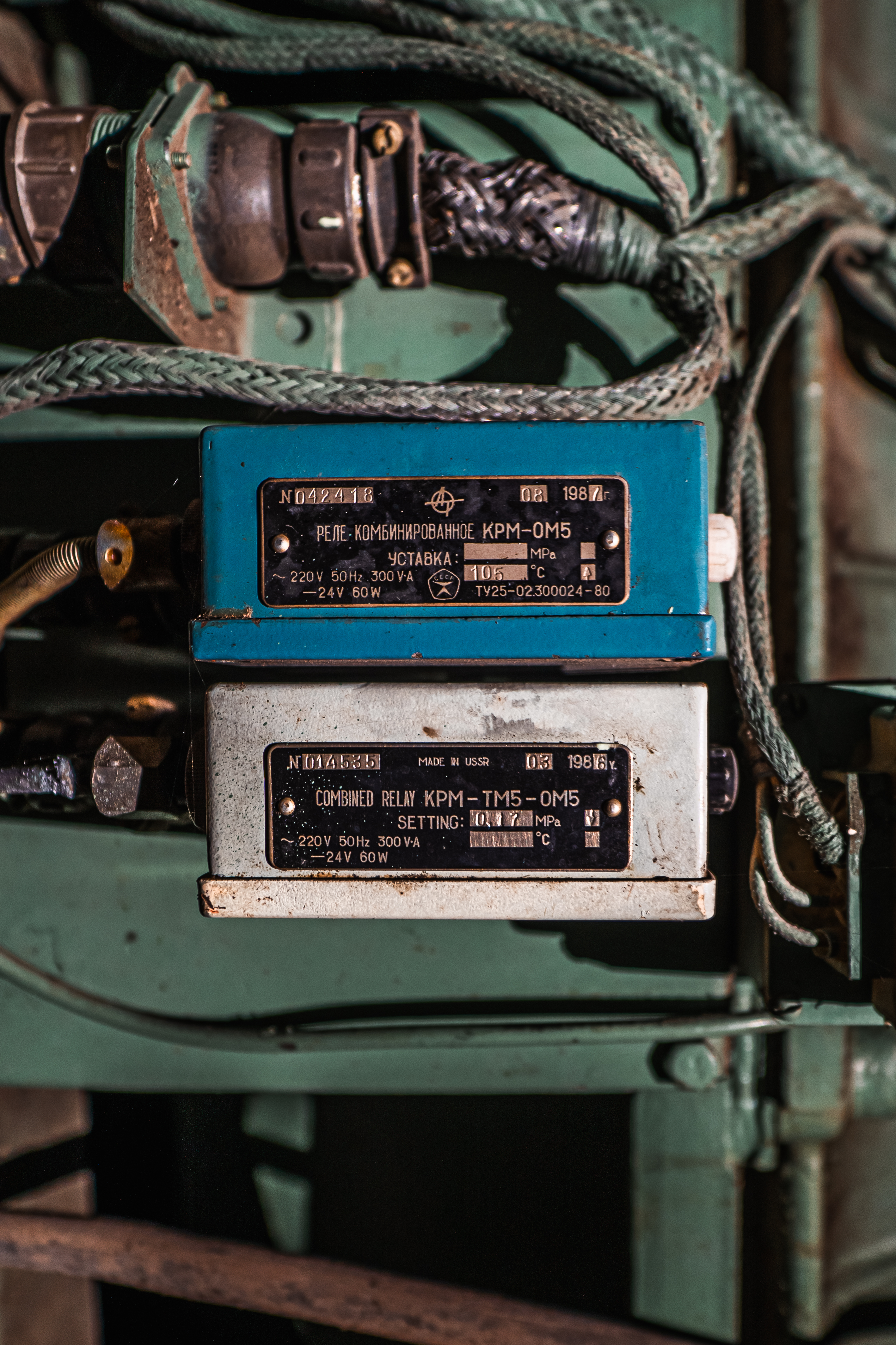 Close-up of two vintage relays, one blue and one white, mounted on a green surface with visible cables and metal connectors.