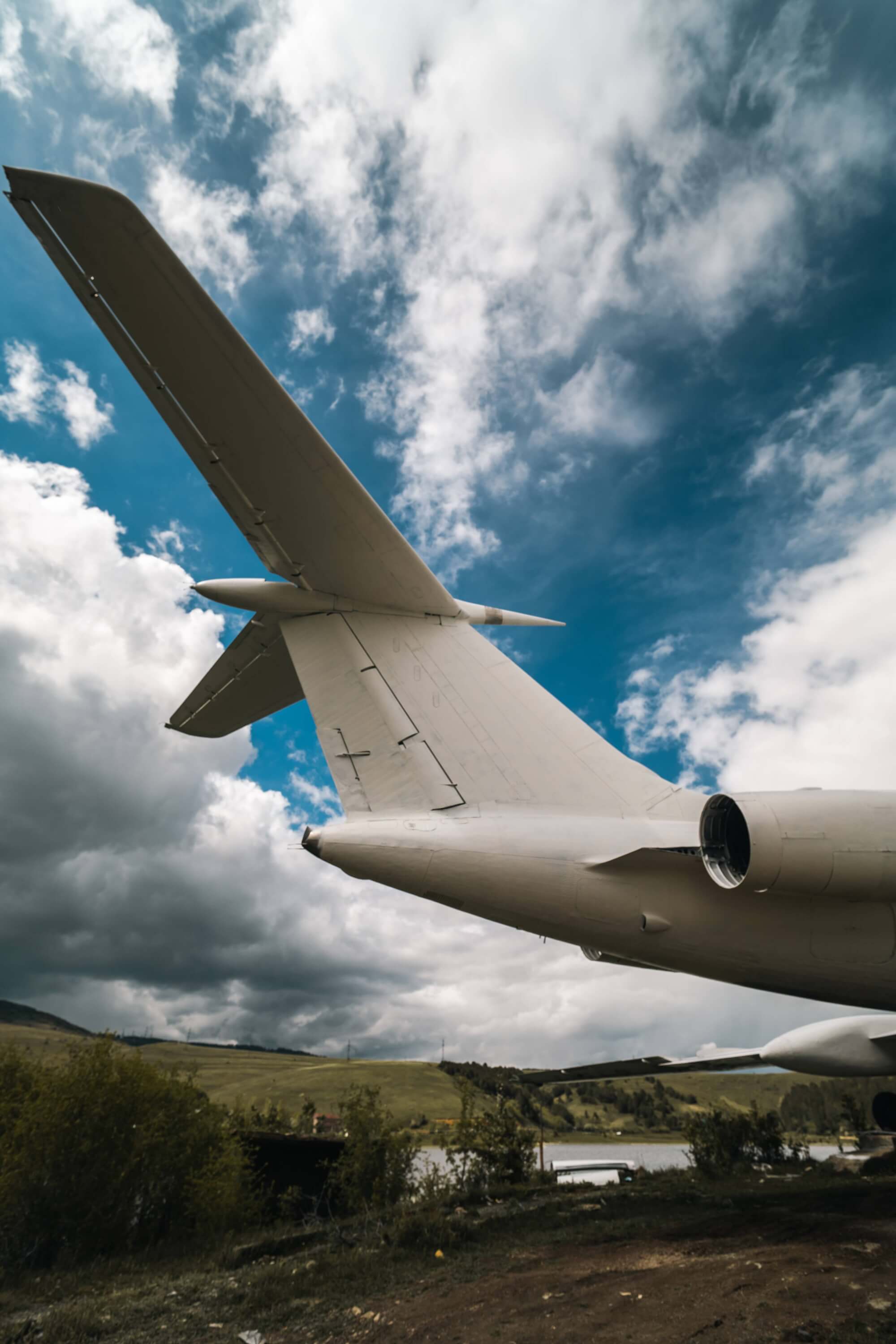 Close-up view of an airplane wing and engine against a cloudy sky, with green hills visible in the background.