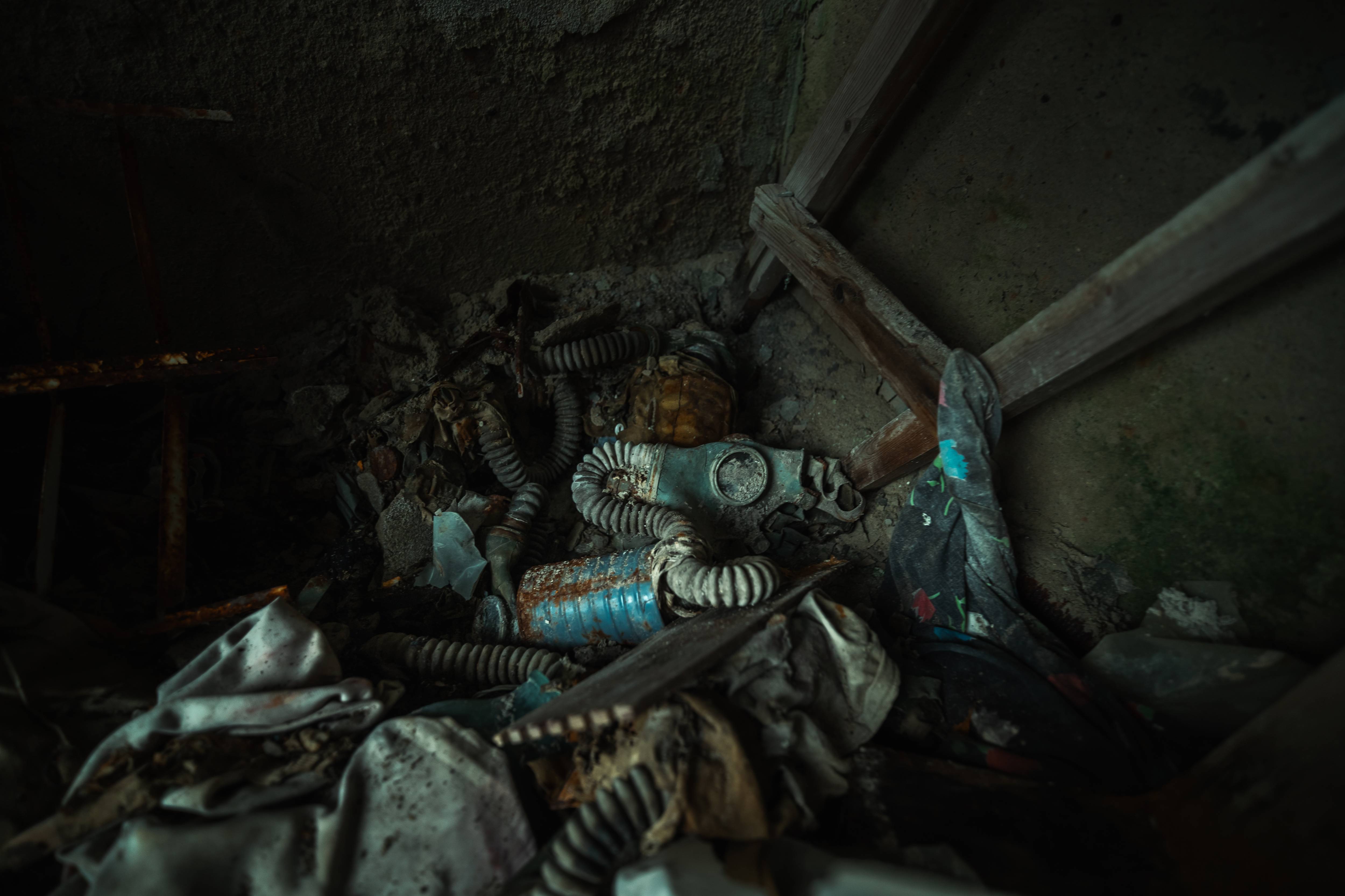 A pile of old gas masks, tubes, and fabrics in a dark corner, surrounded by dust and debris.