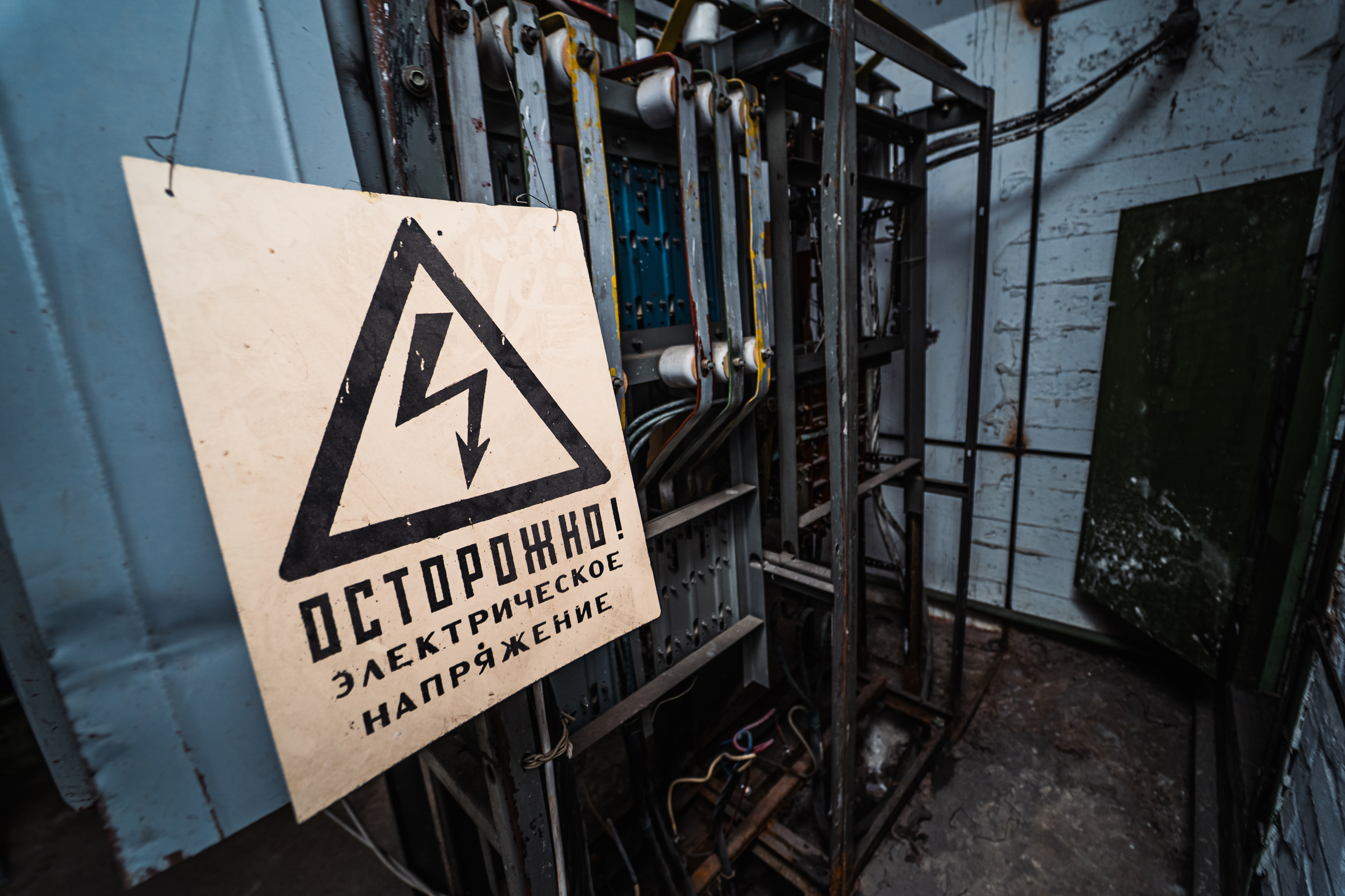 An industrial electrical panel with a caution sign warning of electric danger. The sign features a black lightning bolt inside a triangle, set against a weathered background.