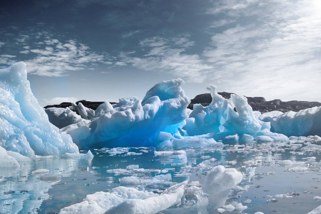 A scenic view of ice formations in water, with a blue hue and soft clouds in the sky.