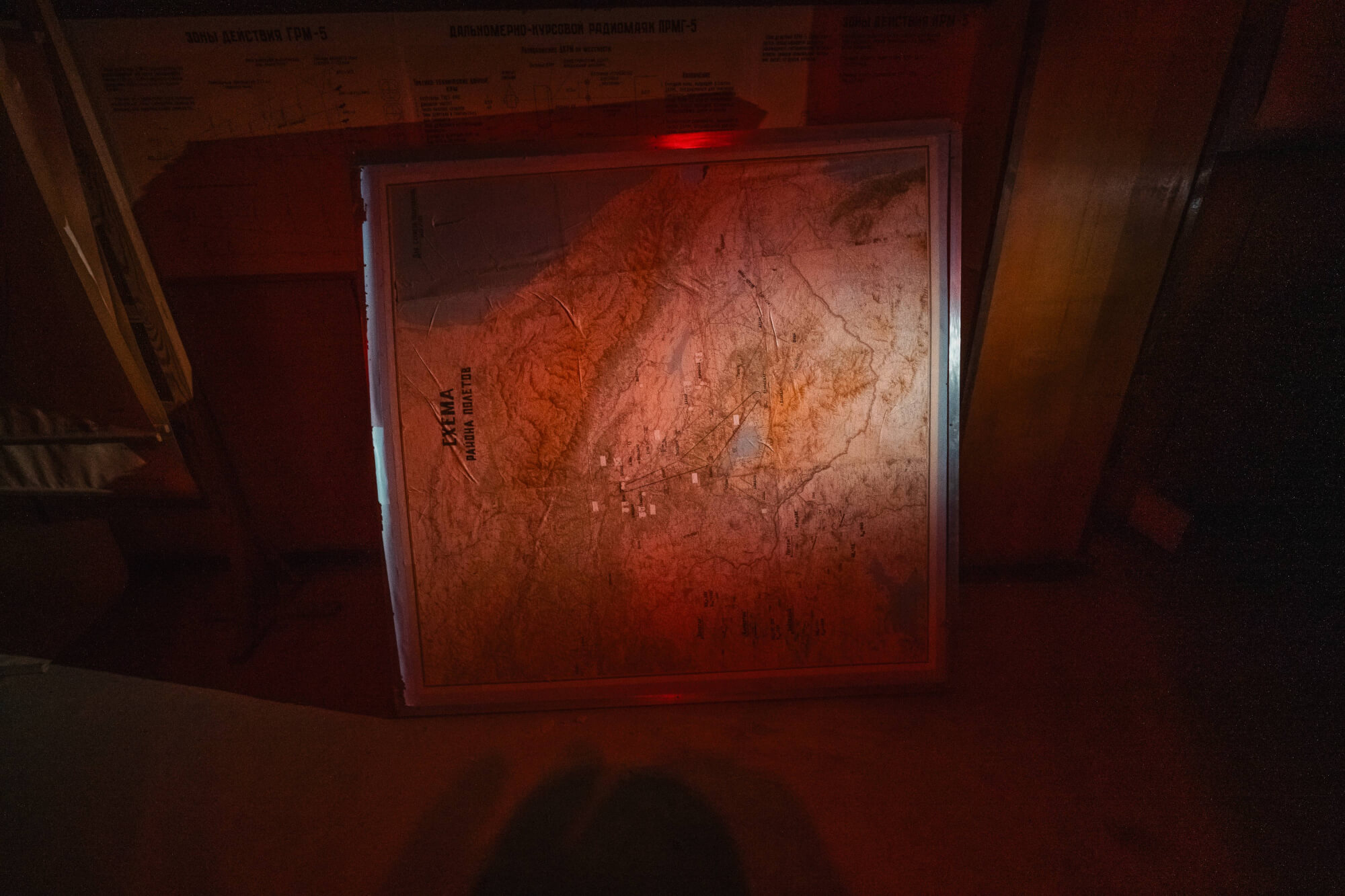 An illuminated topographical map on the floor, partially surrounded by shadows and a warm, red glow. The map features detailed geography with mountains and valleys.