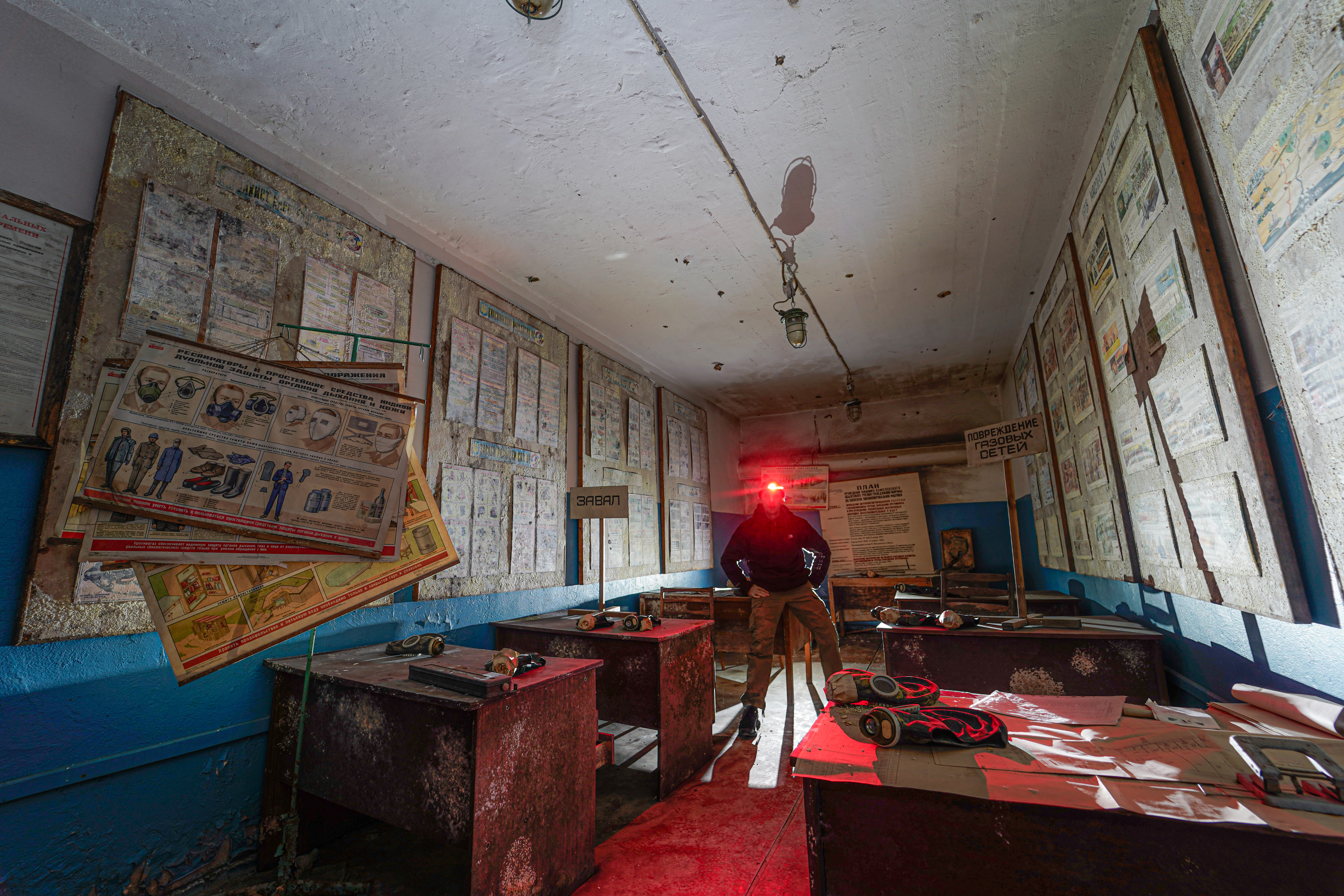 An abandoned room with peeling posters on walls, old desks, and a single figure standing with a red flashlight illuminating the space.