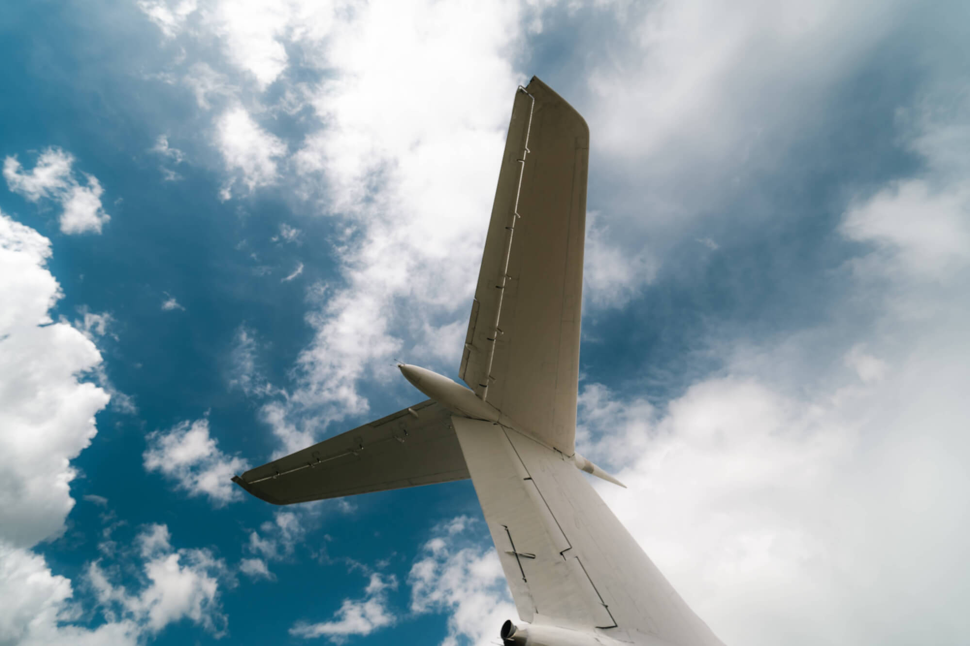 An airplane's tail viewed from below against a blue sky with white clouds.