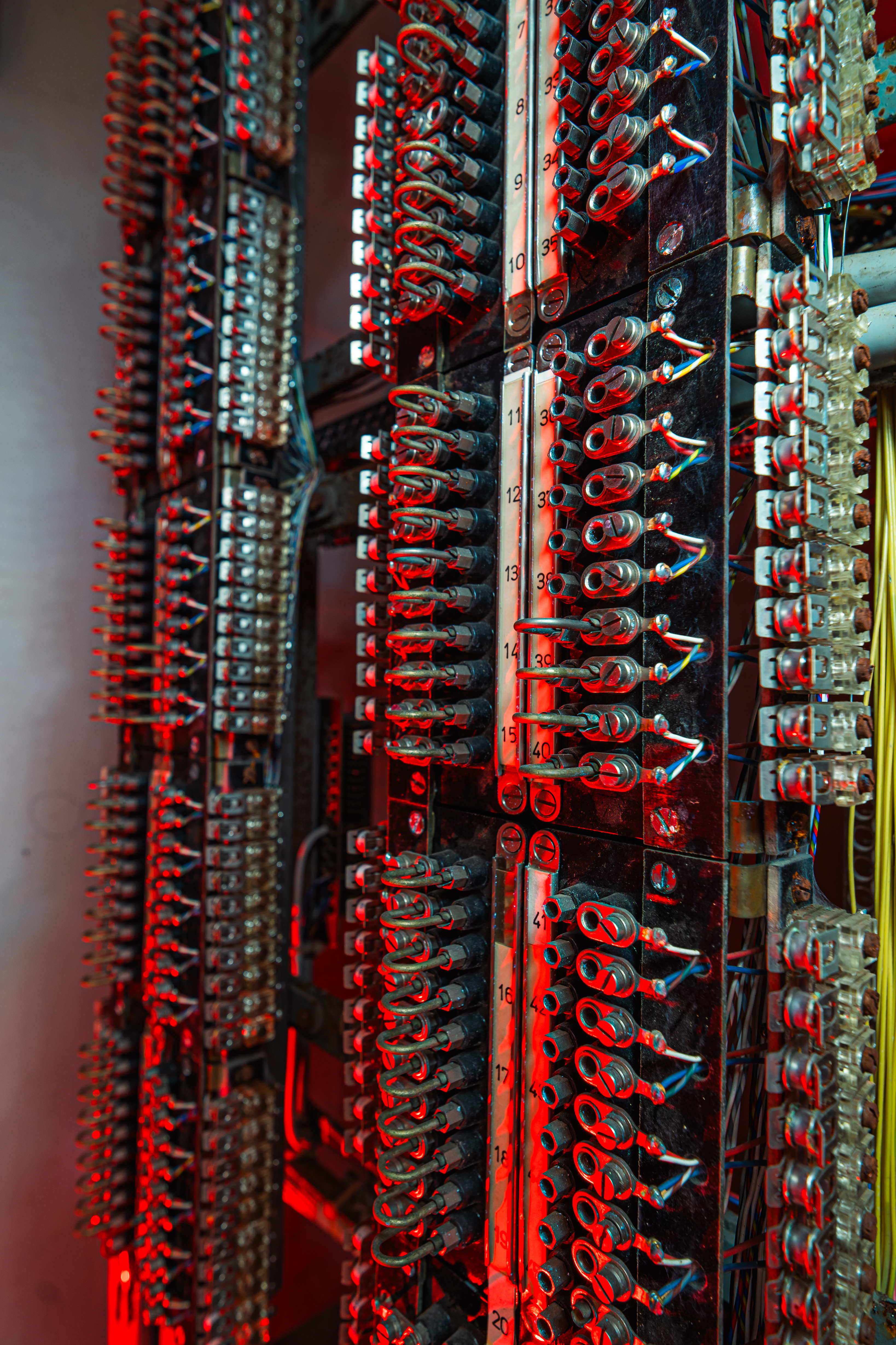 A close-up of a telecommunications panel featuring numerous metallic connectors and colorful wires, illuminated by red lighting, creating a dramatic and nostalgic look.