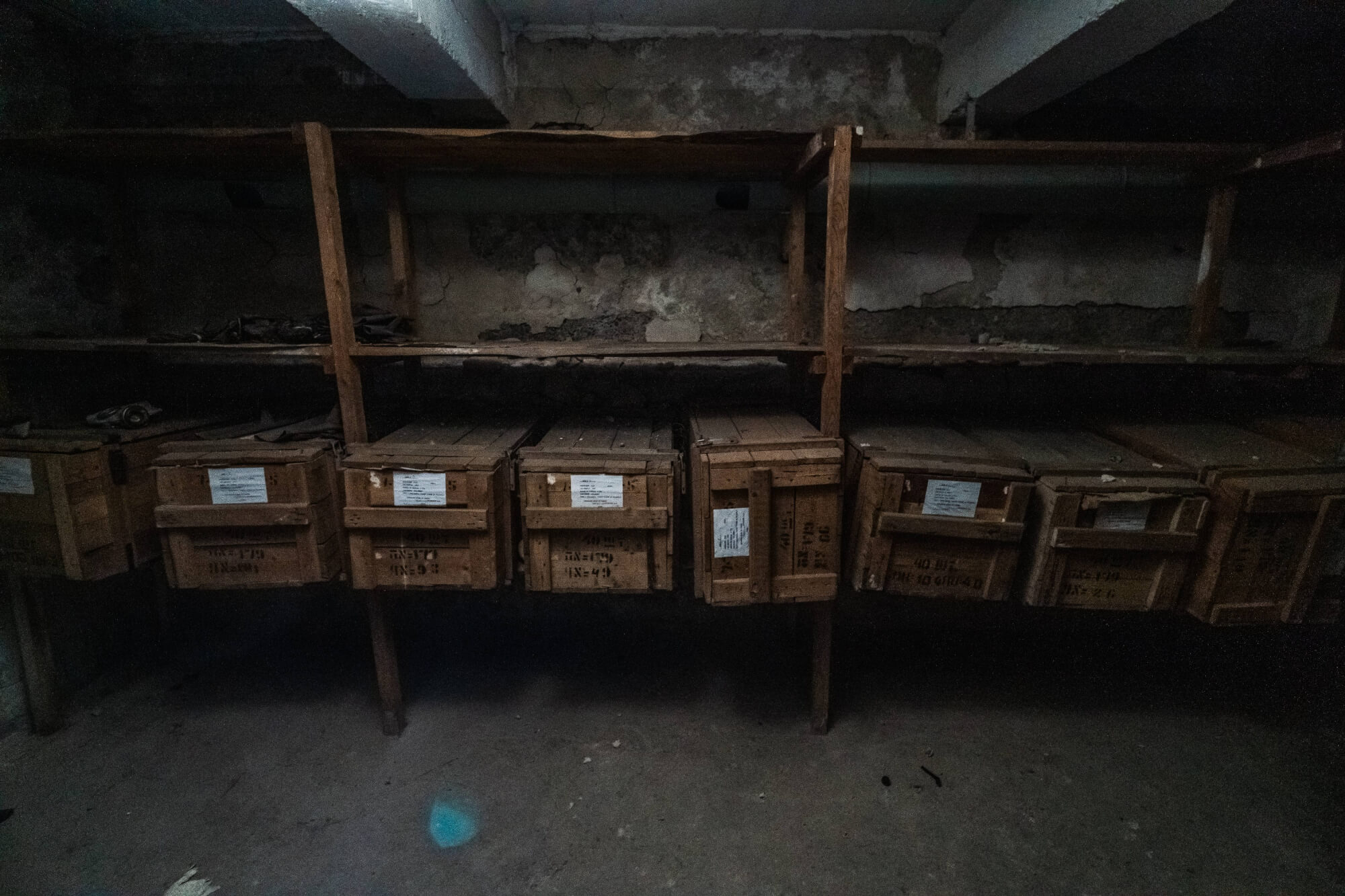 Dimly lit basement with wooden crates on shelves, surrounded by peeling walls, creating a nostalgic and mysterious atmosphere.