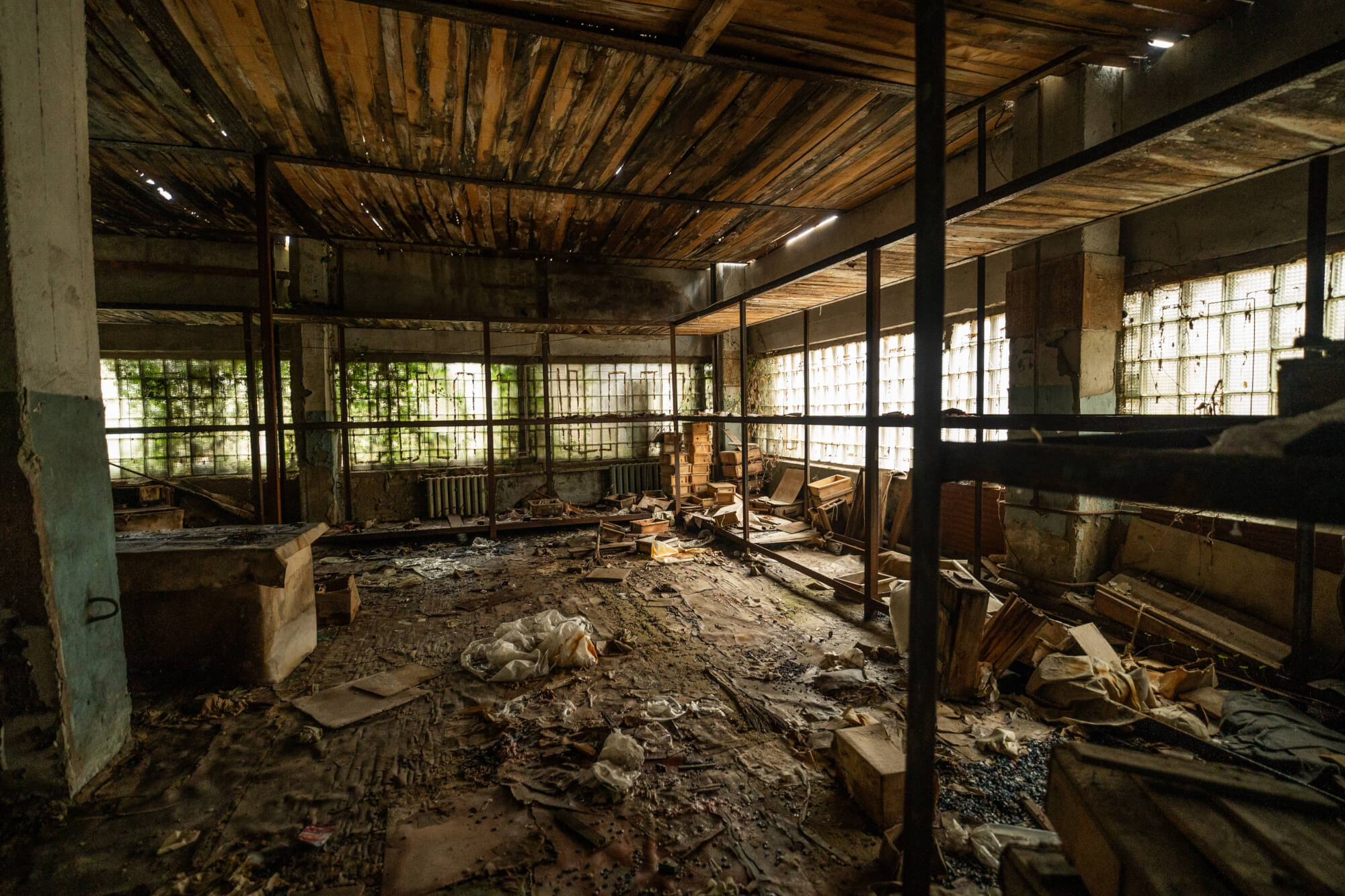An abandoned room with a dusty floor covered in debris and old furniture, sunlight streaming through stained glass windows, and walls partially covered in moss.