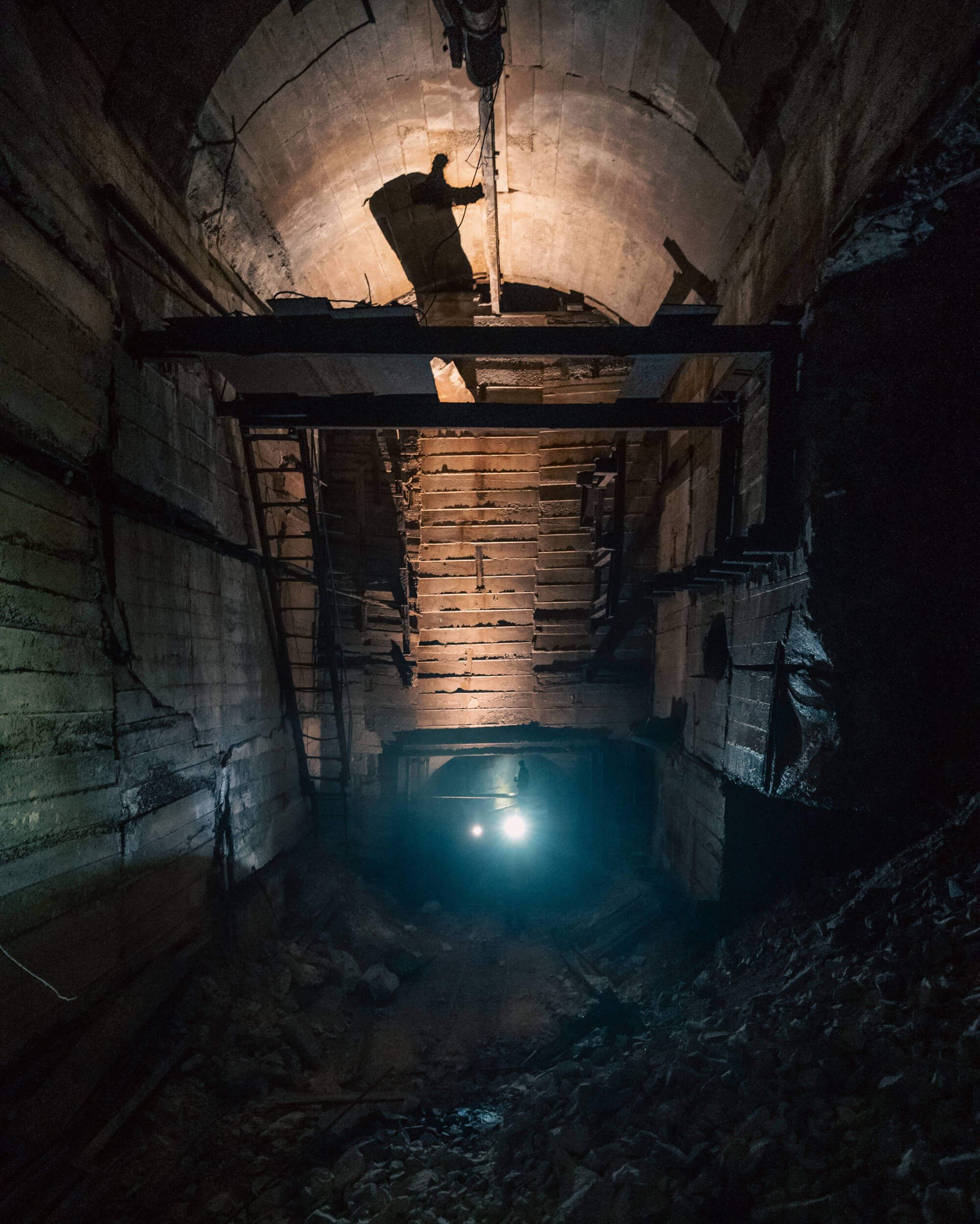 A dimly lit tunnel with rugged concrete walls, showcasing a pile of debris on the ground and a beam of light illuminating the far end.