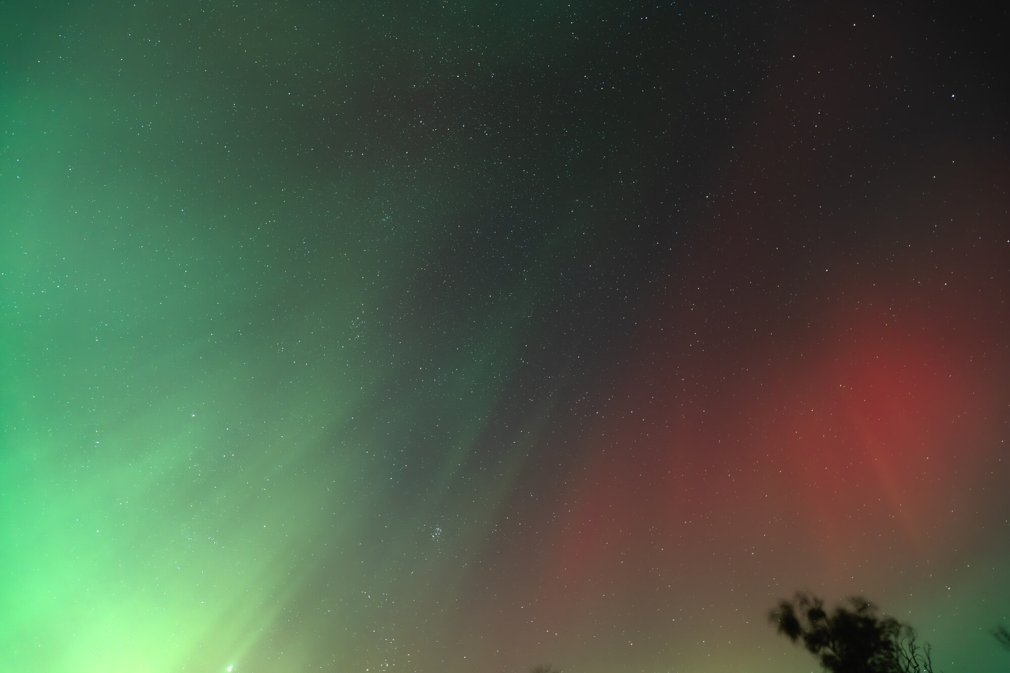 A night sky illuminated by the aurora borealis, featuring green and red lights with numerous stars scattered throughout.