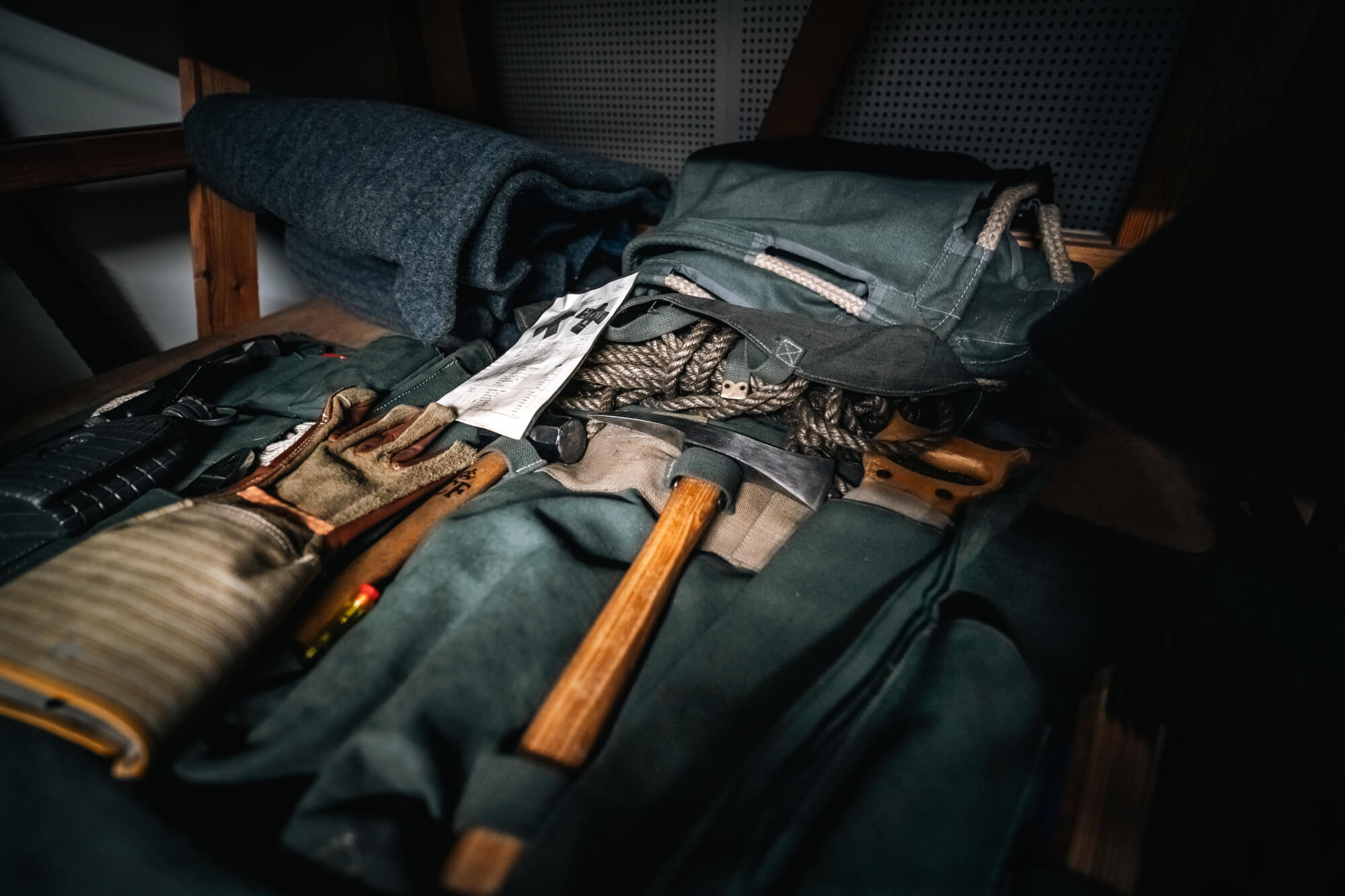 A close-up view of outdoor gear including a wooden-handled axe, gloves, ropes, and a piece of paper, resting on a wooden surface.