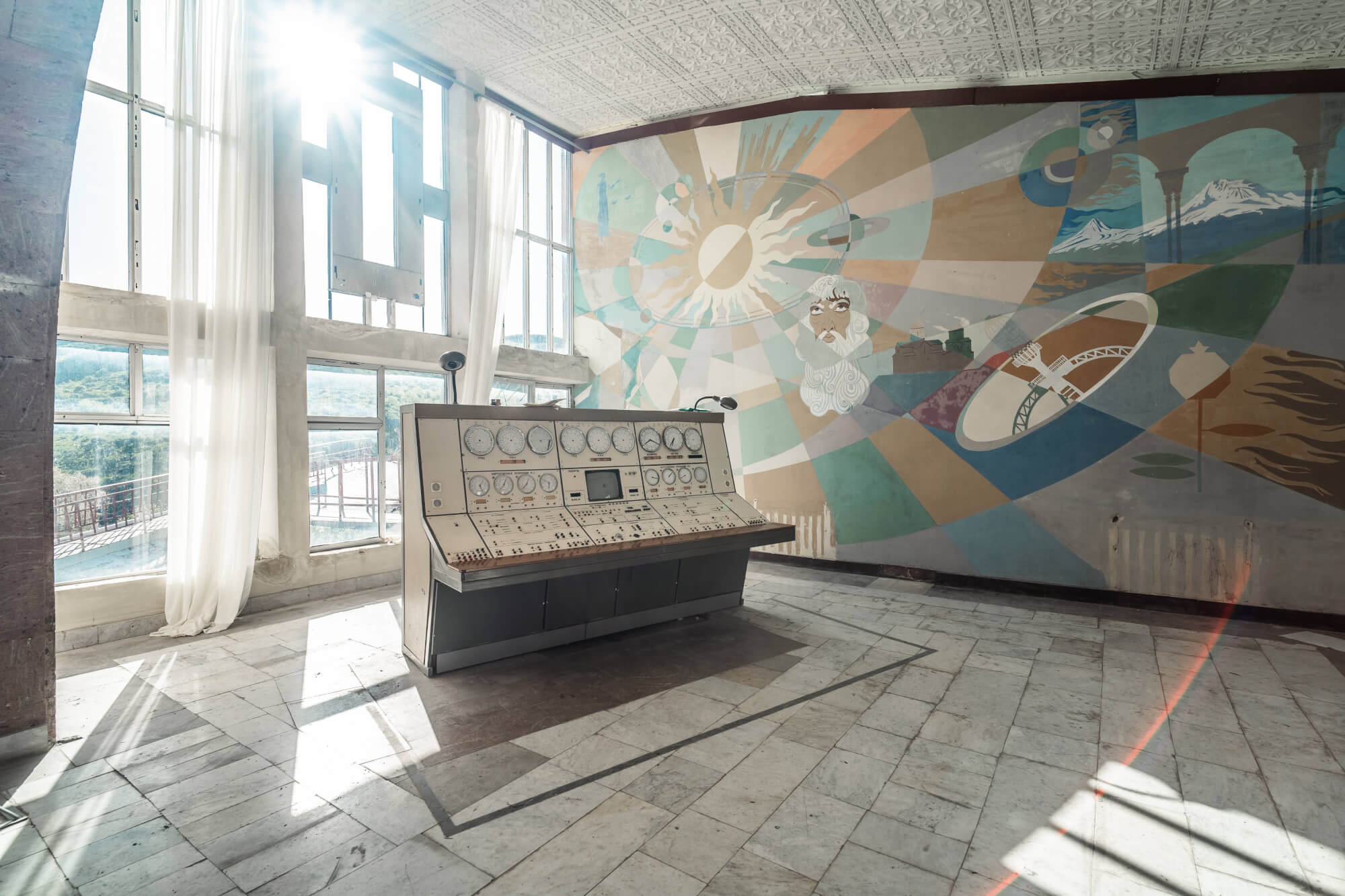A vintage control panel in a sunlit room with tall windows, surrounded by a colorful abstract mural on the wall. The floor is made of marble tiles, and soft white curtains are visible blowing gently.
